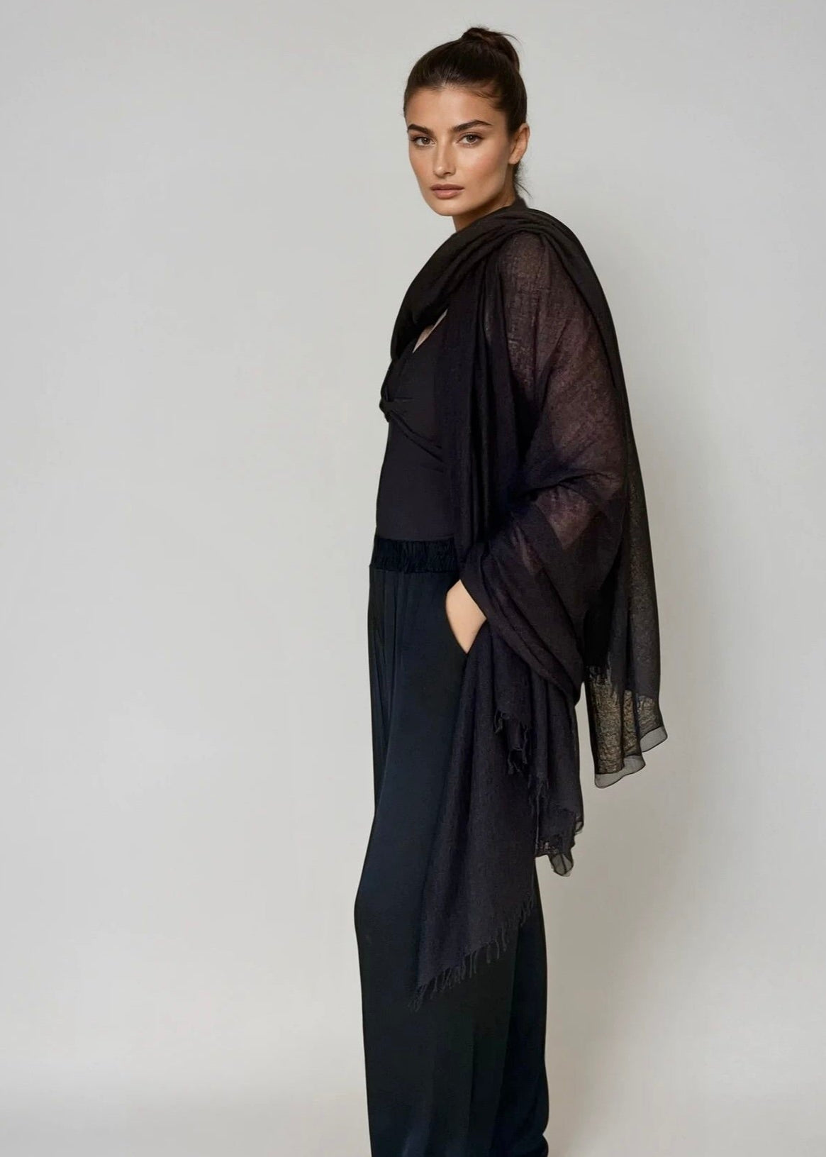 Woman wearing a black outfit with a extra large matching cashmere black shawl against a plain background
