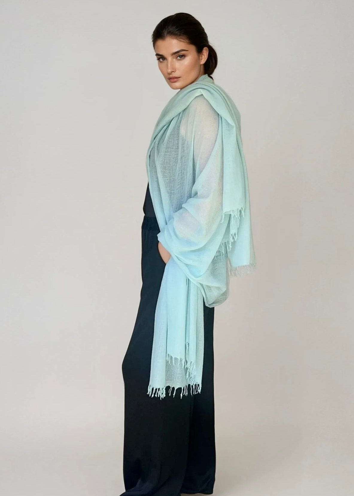 Woman wearing a extra large, cashmere opal blue shawl on a plain background.