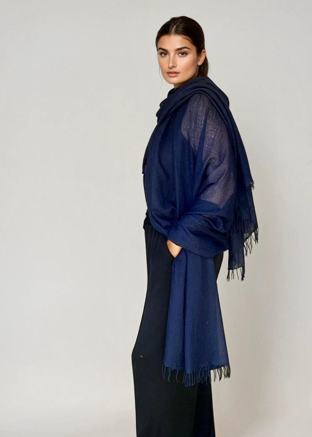 Woman wearing a navy blue extra large cashmere shawl on a plain background