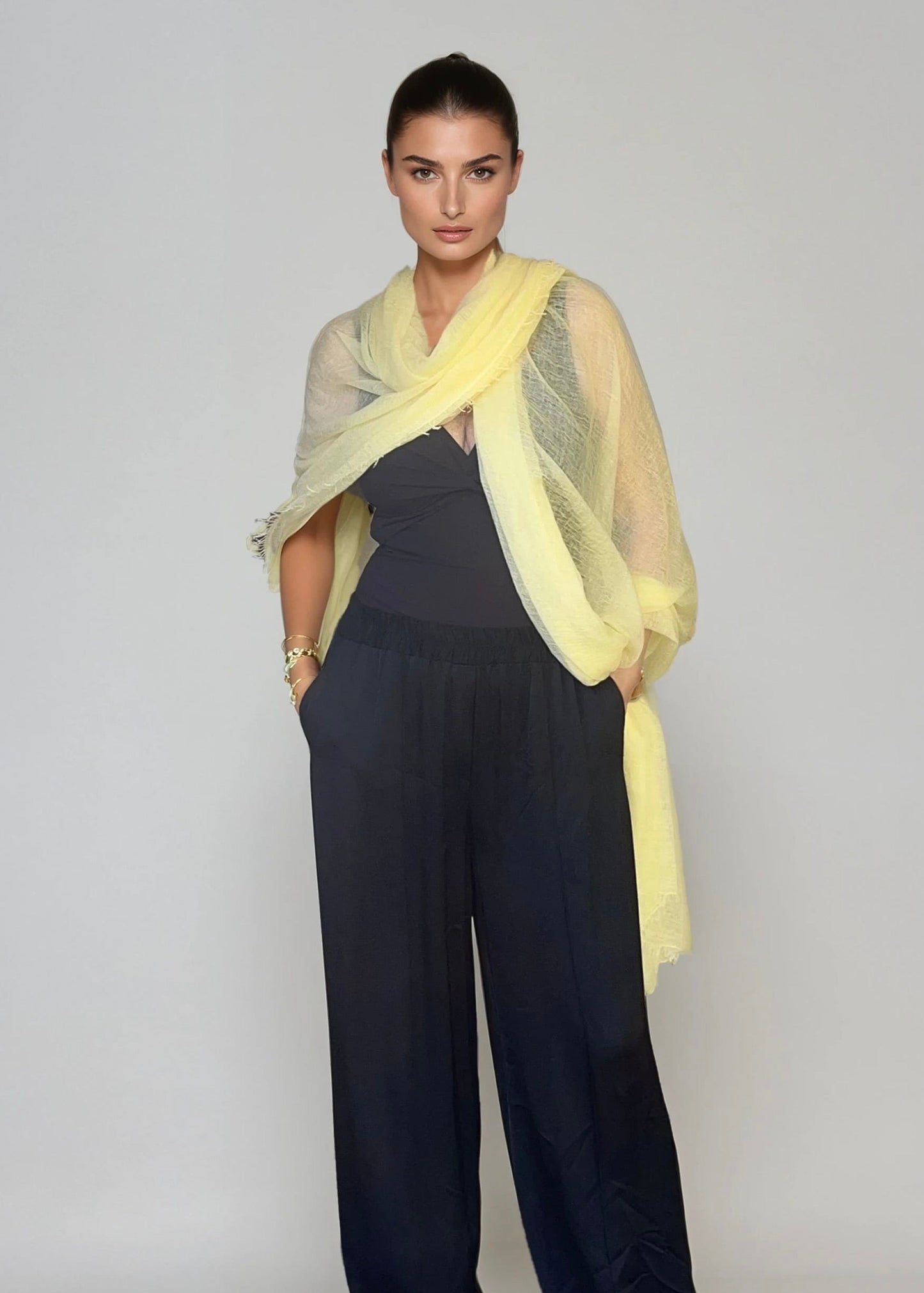 Woman wearing a light yellow, extra large cashmere wrap in a studio.