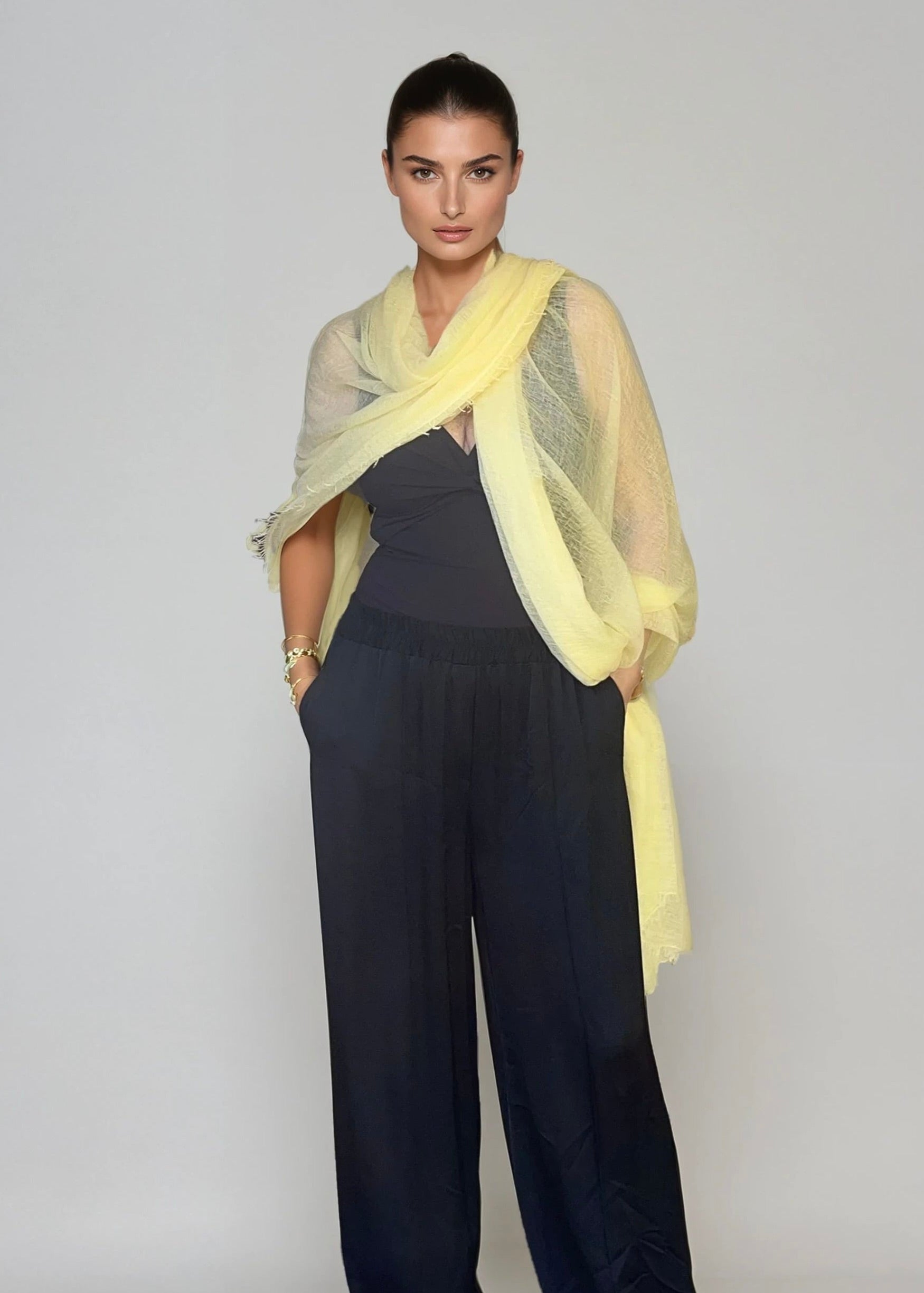 Woman wearing a light yellow, extra large cashmere wrap in a studio.