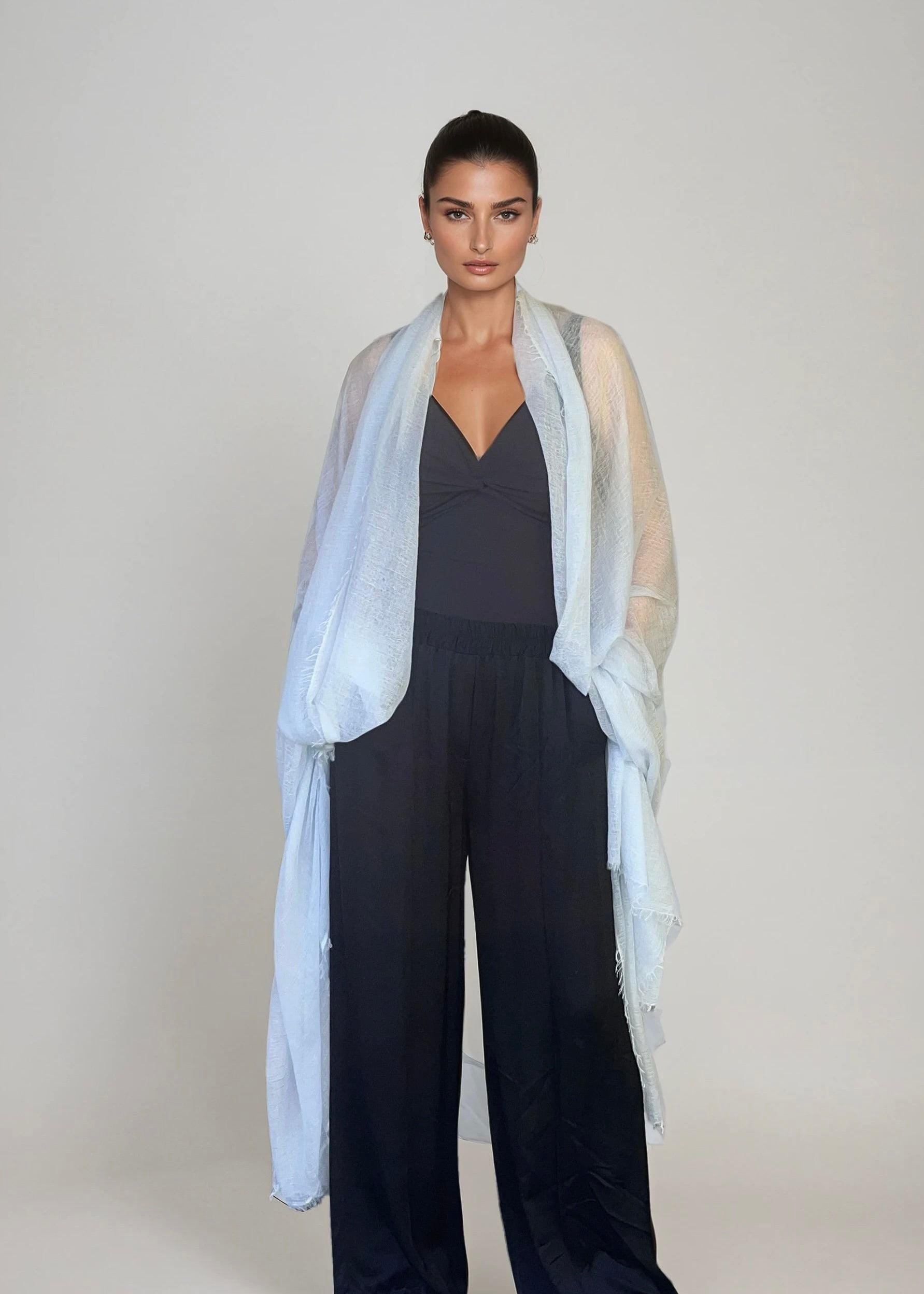 Woman wearing a light blue , extra large cashmere shawl in a studio.