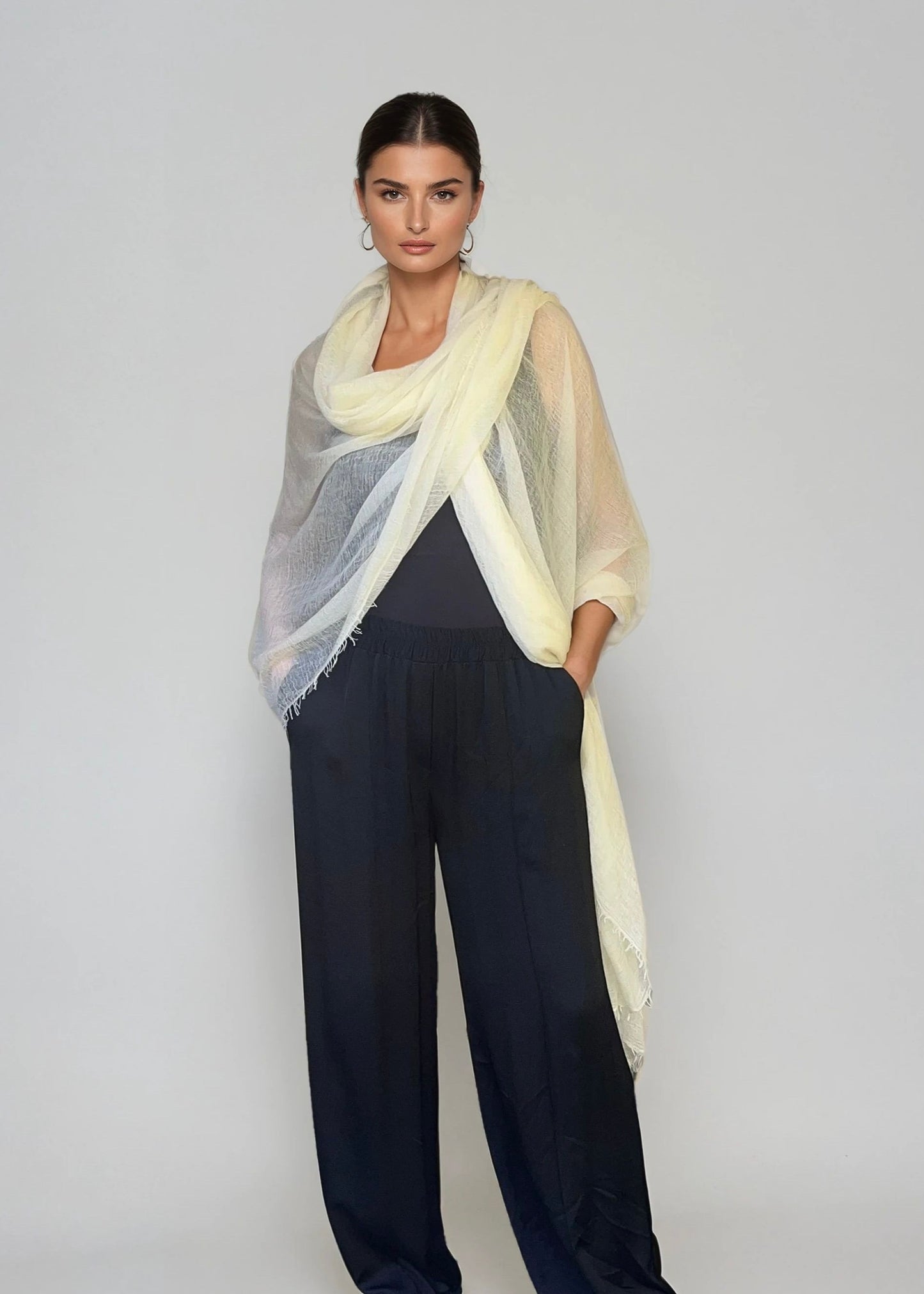 Woman wearing a light weight  extra large cashmere scarf over a black top and black pants on a white background