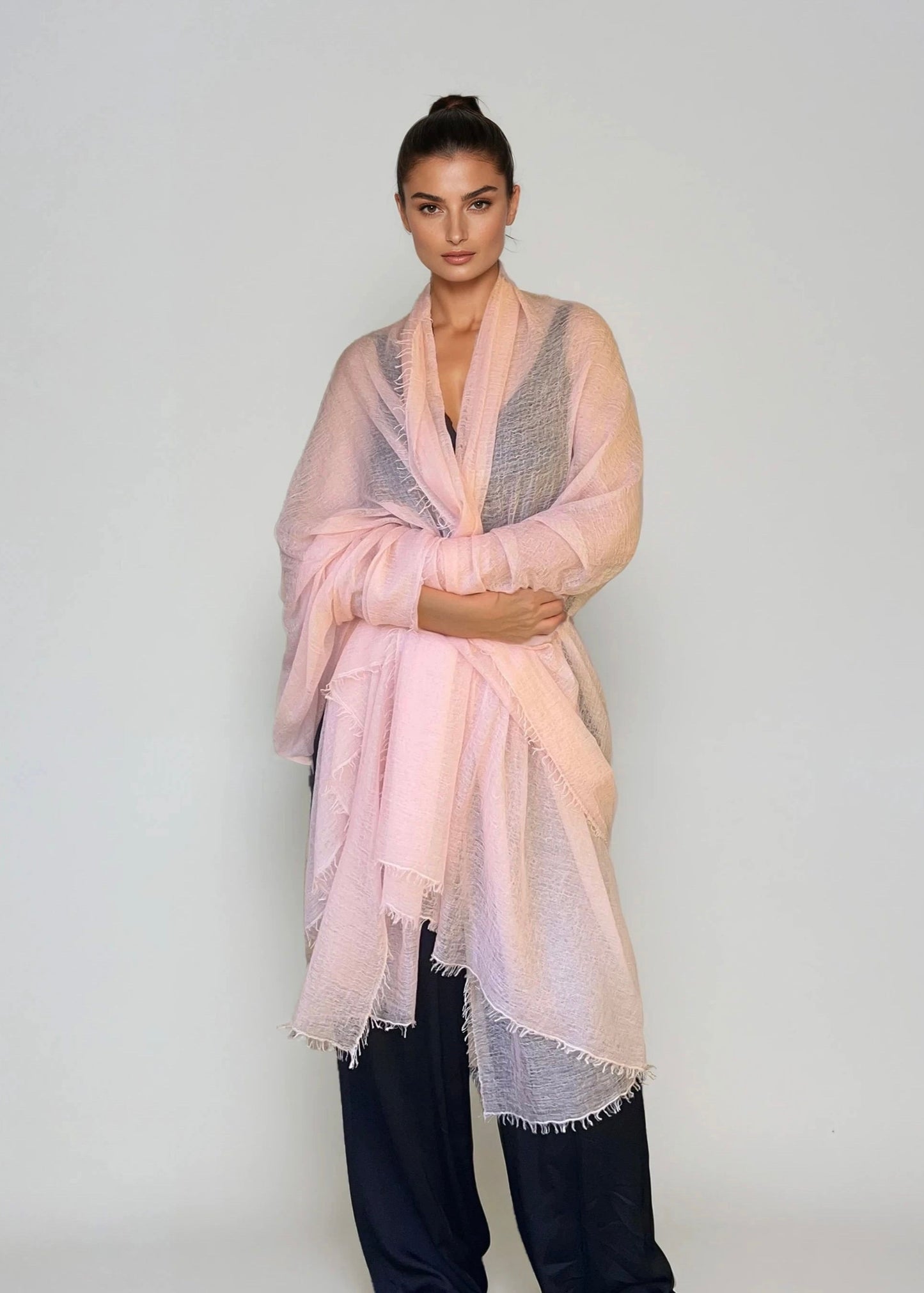 Woman wearing a extra large, light pink cashmere wrap n a studio.