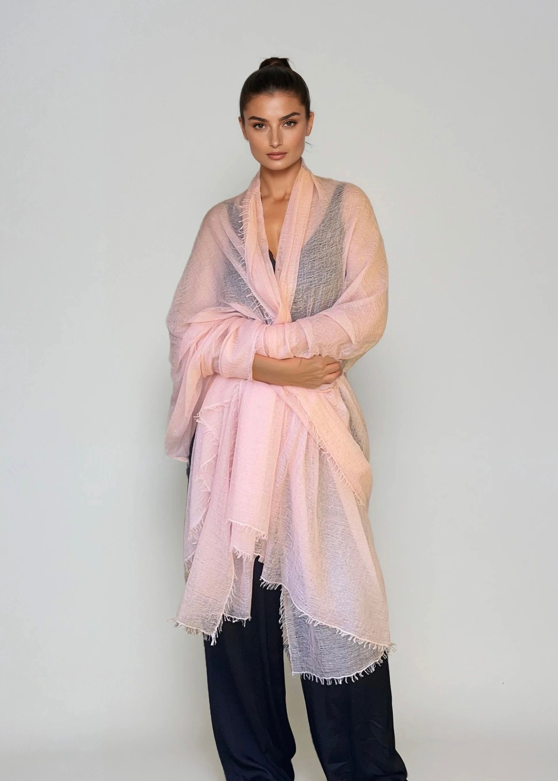 Woman wearing a extra large, light pink cashmere wrap n a studio.