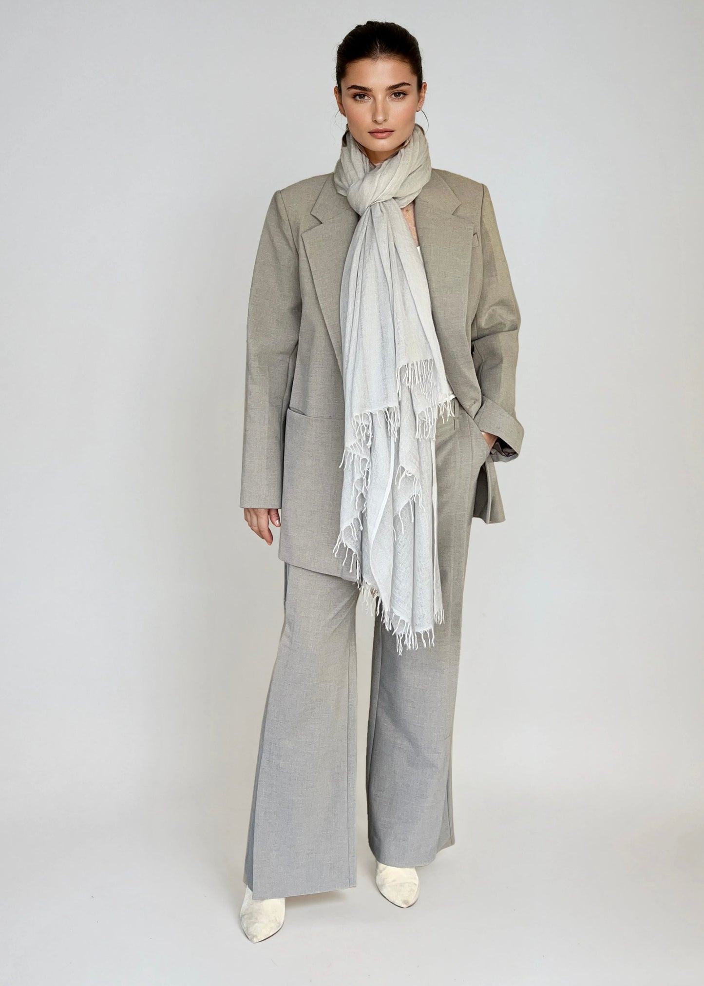 Woman wearing a gray suit with a soft grey scarf on a plain background