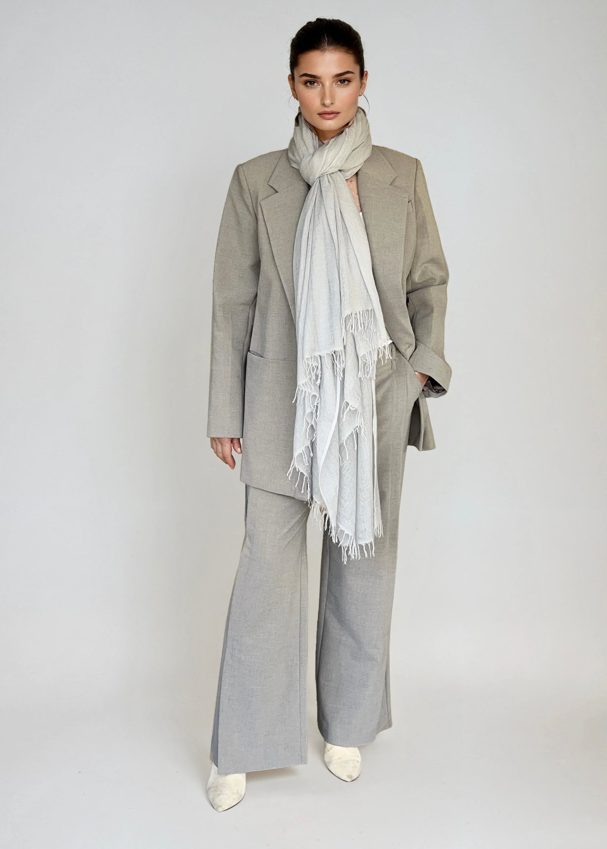 Woman wearing a gray suit with a soft grey scarf on a plain background