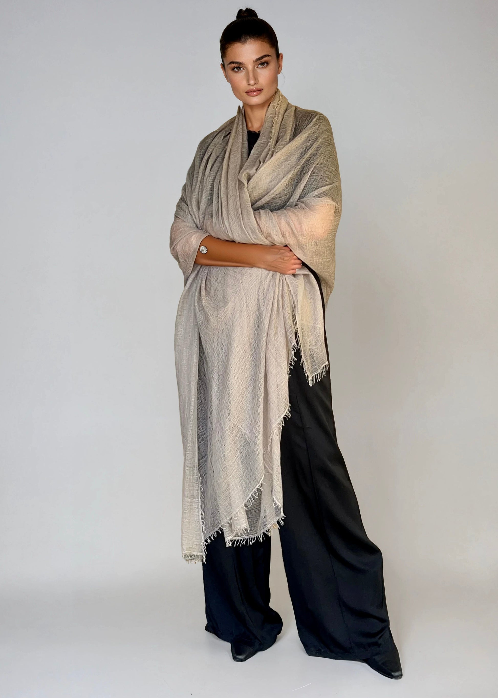 Woman wearing a extra large soft grey cashmere shawl and black pants on a white background