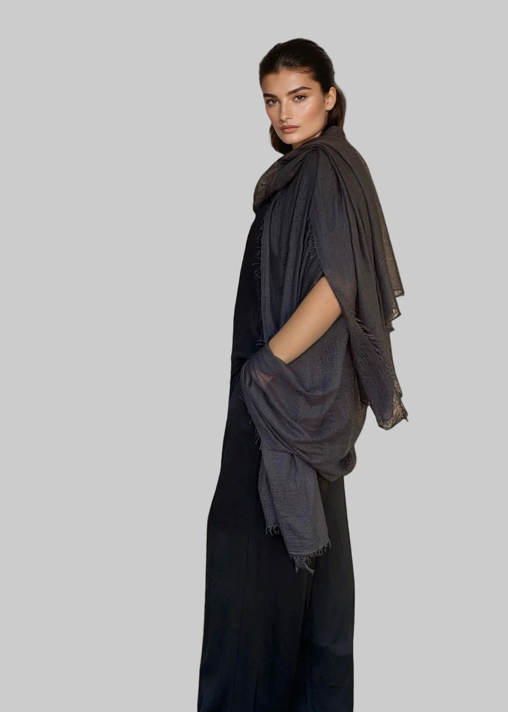 Woman wearing a extra large cashmere charcoal shawl draped over her shoulders against a white background
