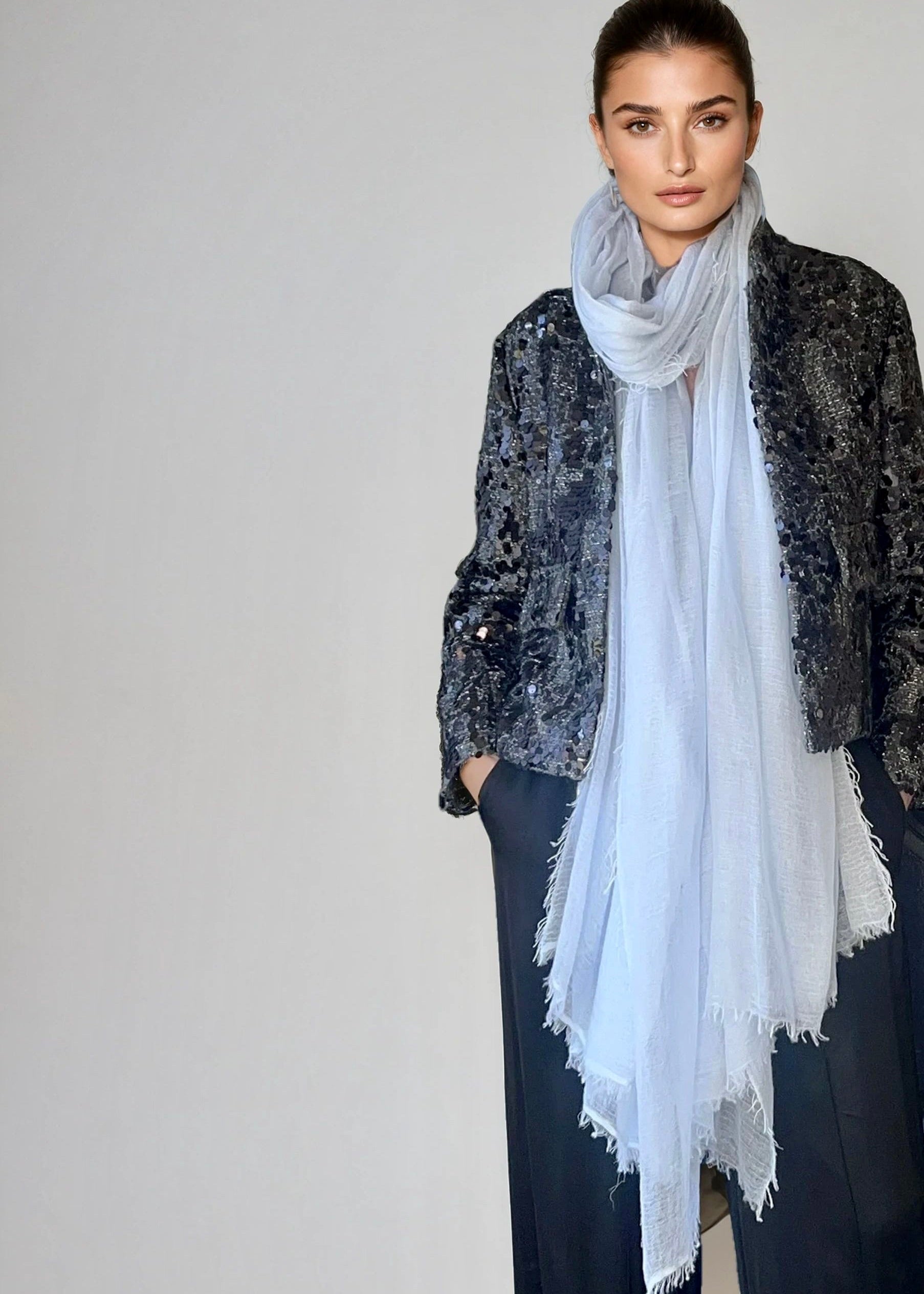 Woman wearing a light blue , extra large cashmere scarf in a studio.