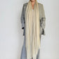 Woman wearing a long beige scarf and gray coat against a plain background