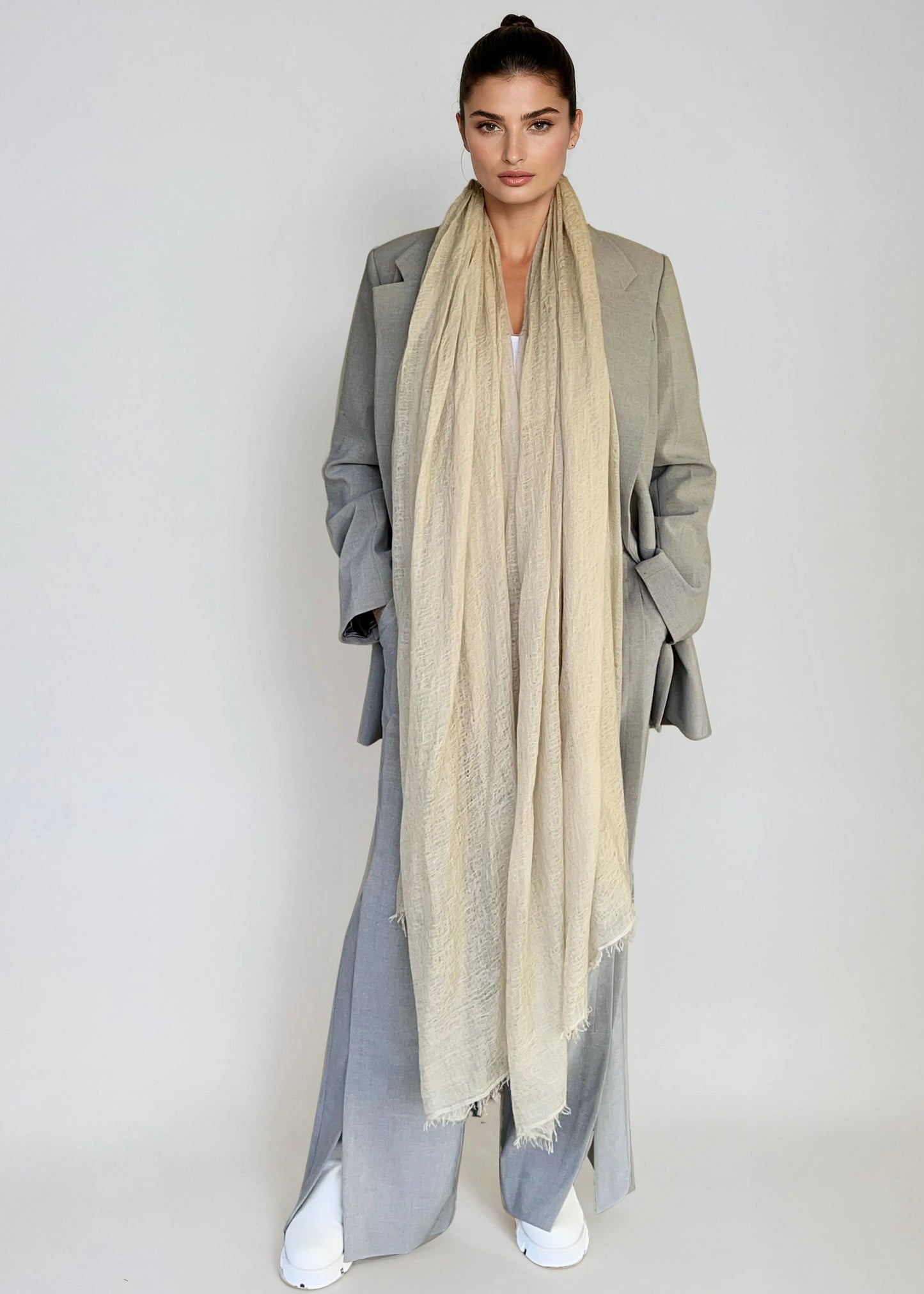 Woman wearing a long beige scarf and gray coat against a plain background