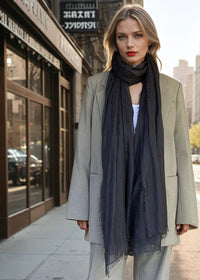 Woman standing on a city street wearing a gray suit and a extra large cashmere charcoal scarf.