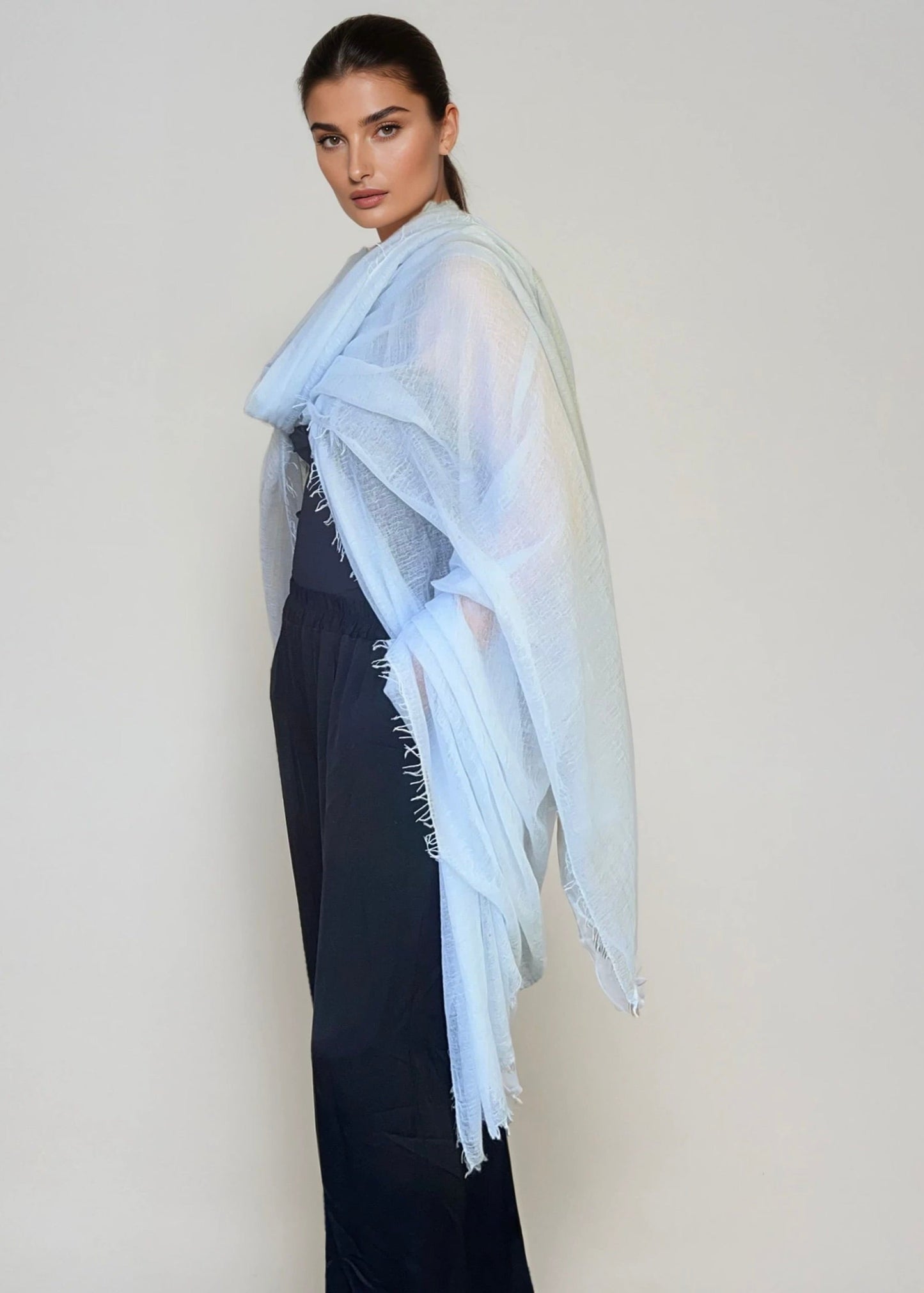 Woman wearing a light blue scarf with fringe on a plain background