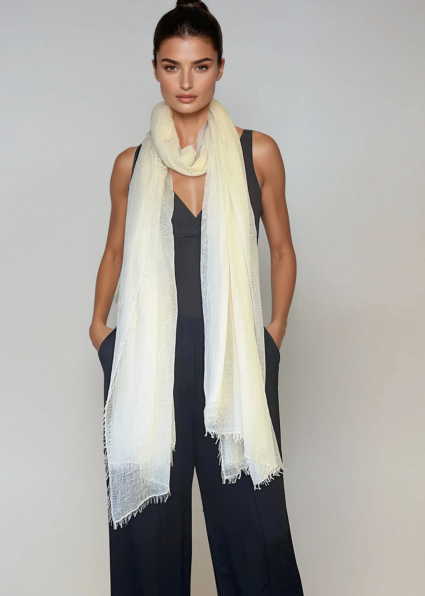 Woman wearing a white scarf and black jumpsuit on a plain background