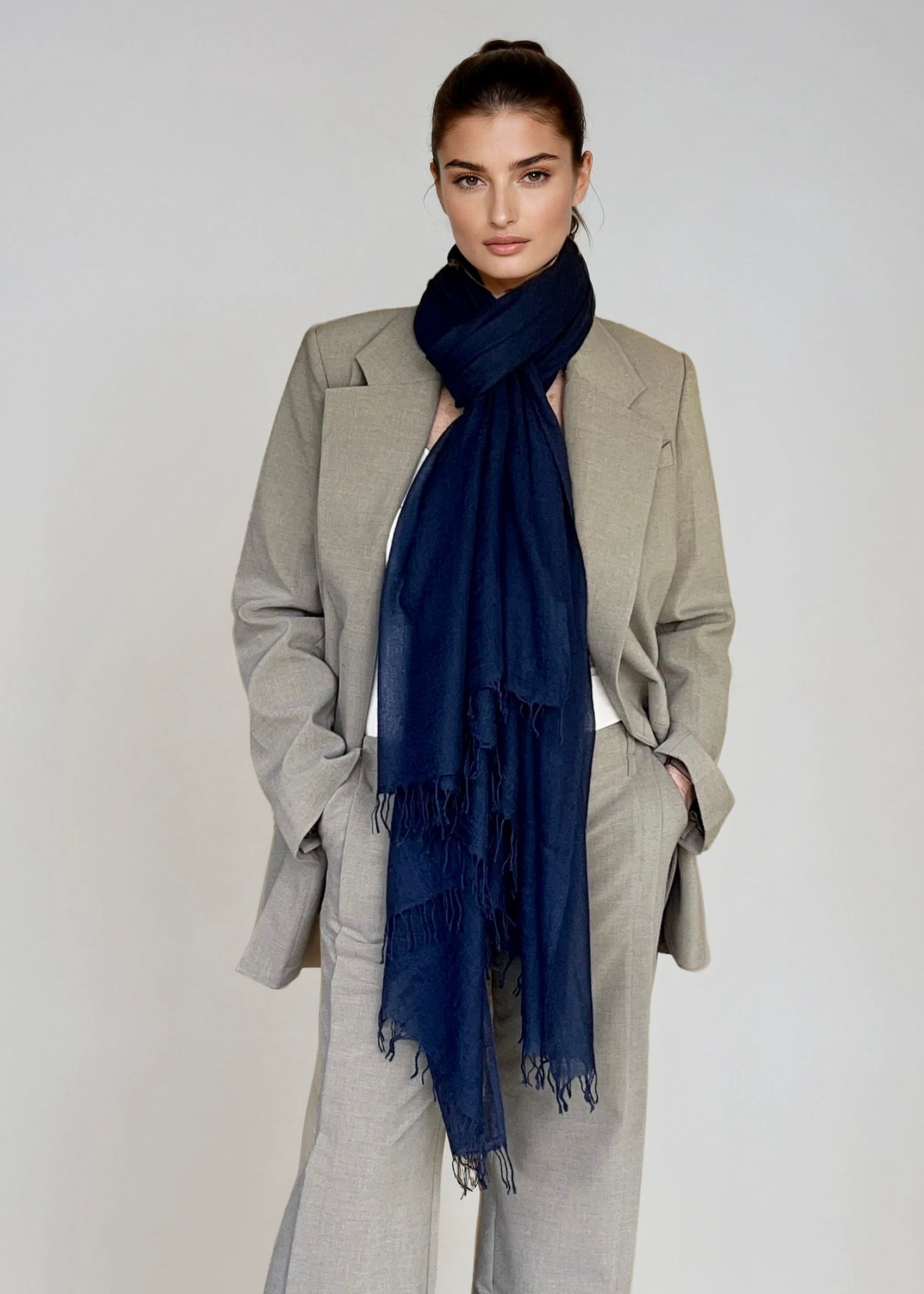 Woman wearing a gray suit with a navy scarf on a plain background