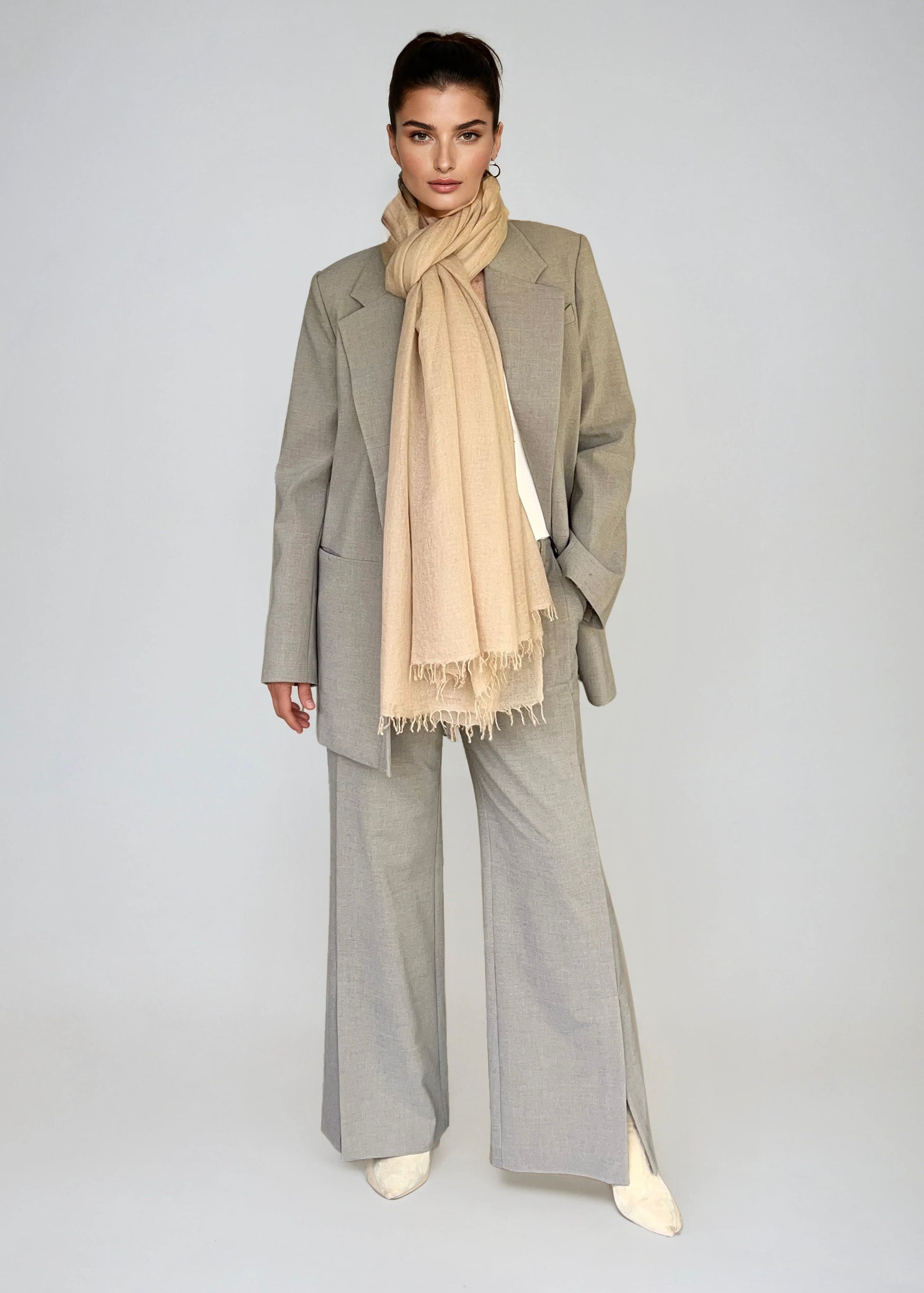 Person wearing a gray coat and pants with a beige scarf on a plain background