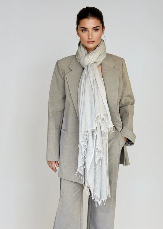 Woman wearing a gray suit with a soft grey scarf on a plain background