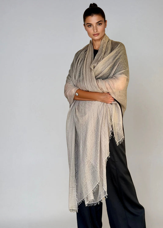 Woman wearing a extra large soft grey cashmere shawl and black pants on a white background