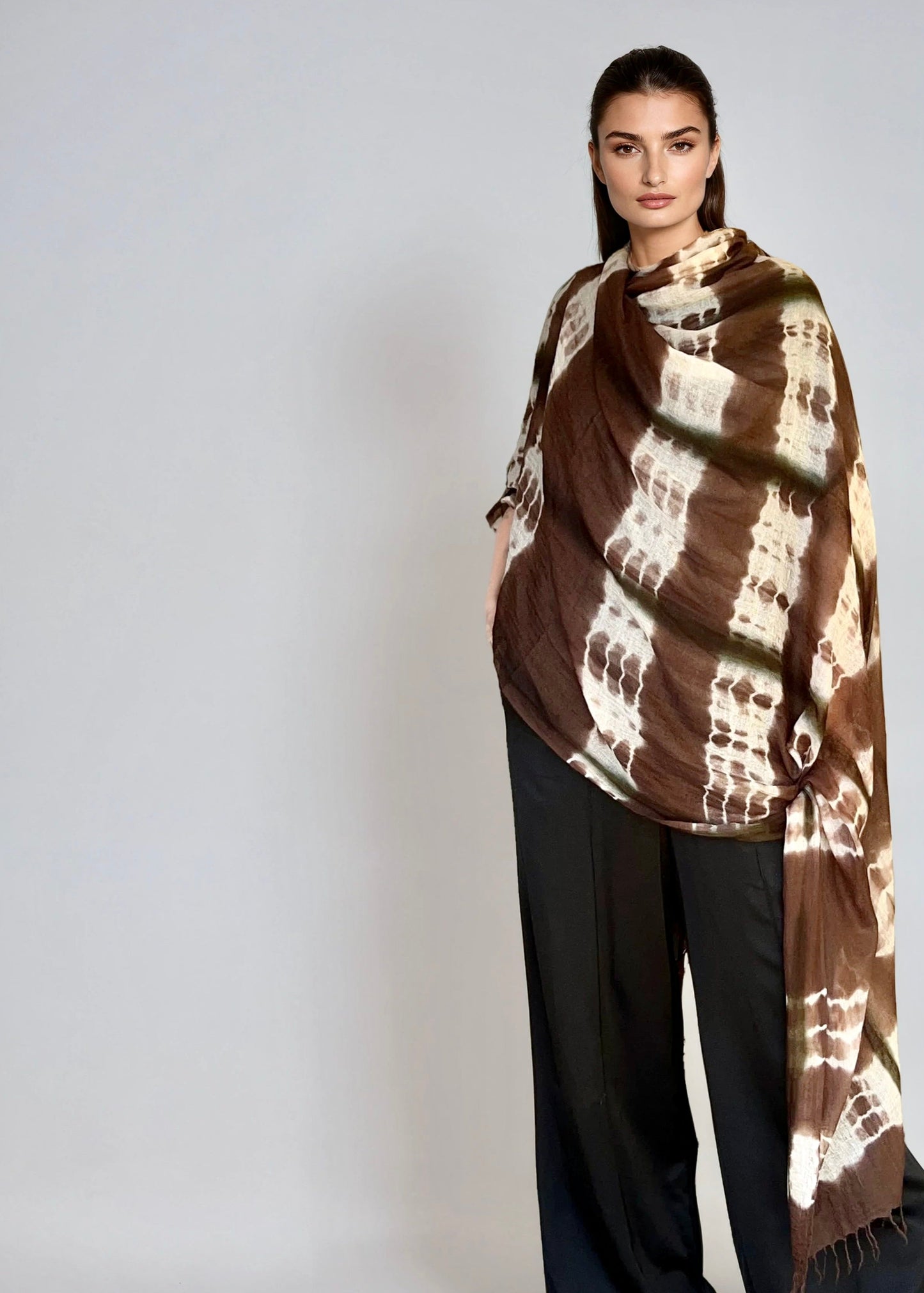 Woman wearing a cashmere extra large wrap in brown and white patterned on a plain background