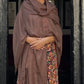 Woman wearing a brown shawl over a patterned dress standing in front of a dark wooden door.