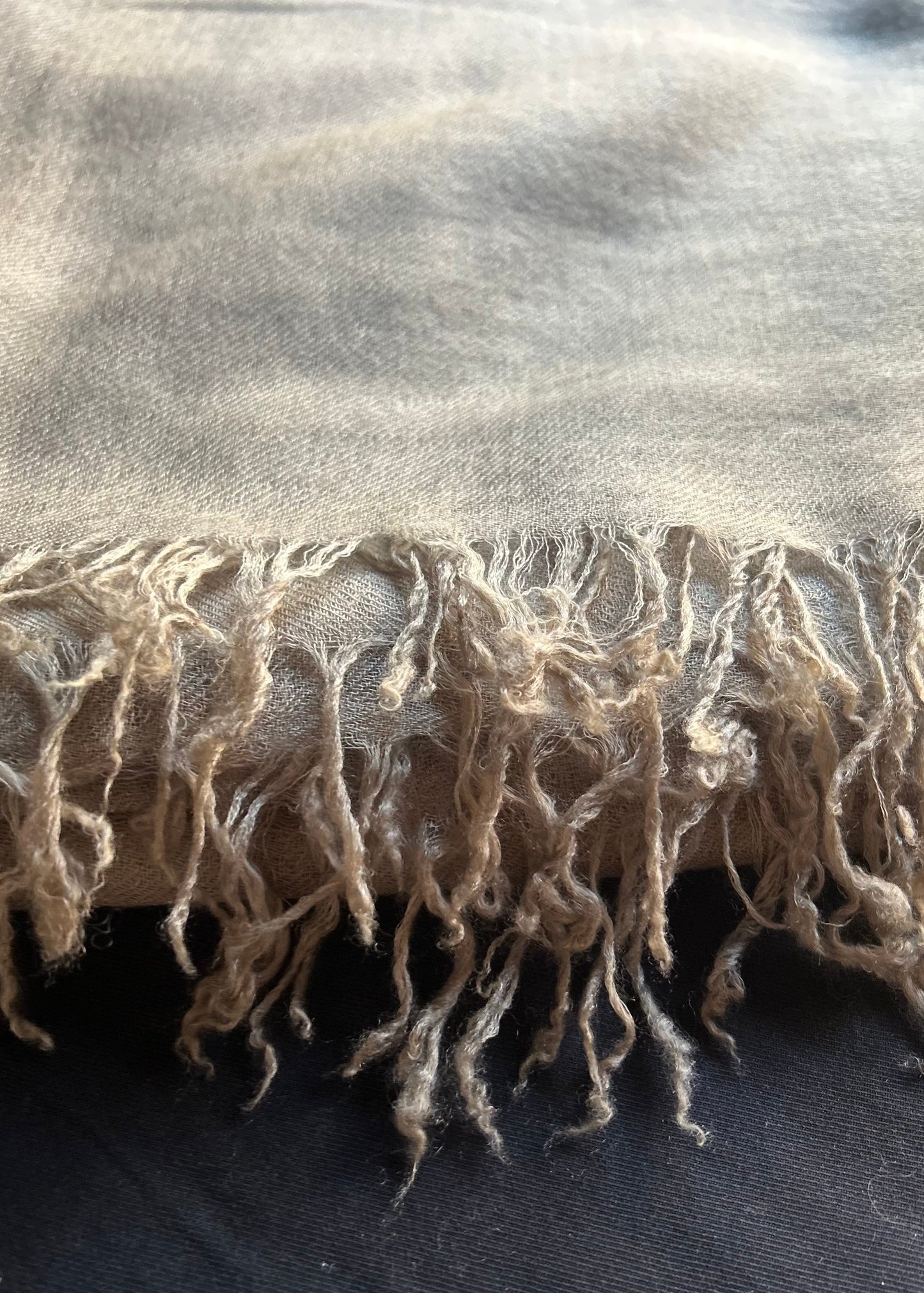 Close-up of a beige scarf with frayed edges on a dark surface