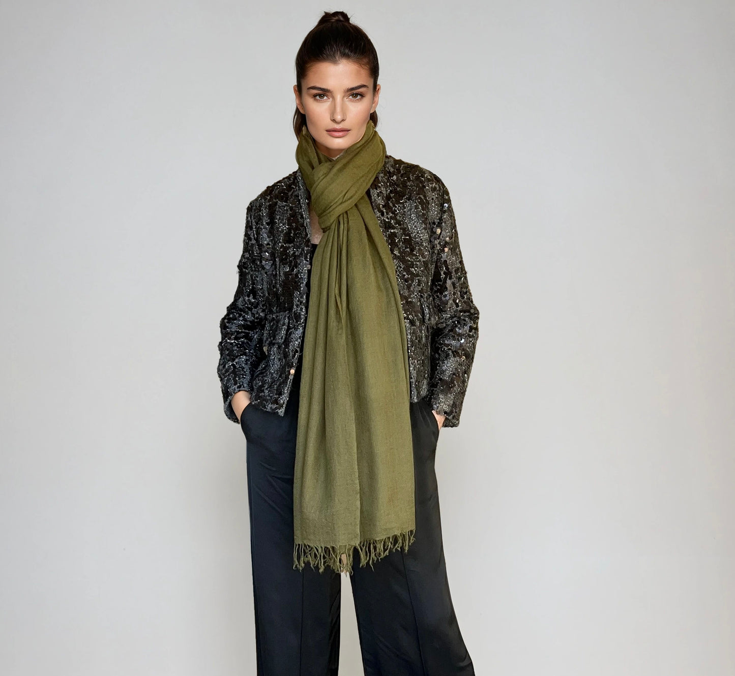 Woman wearing a green scarf and black patterned jacket on a white background