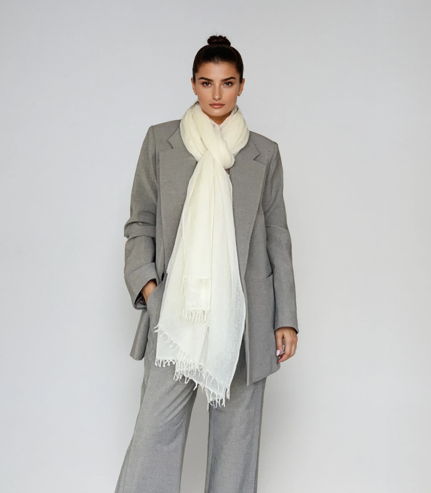 Woman wearing a gray suit with a white scarf on a plain background