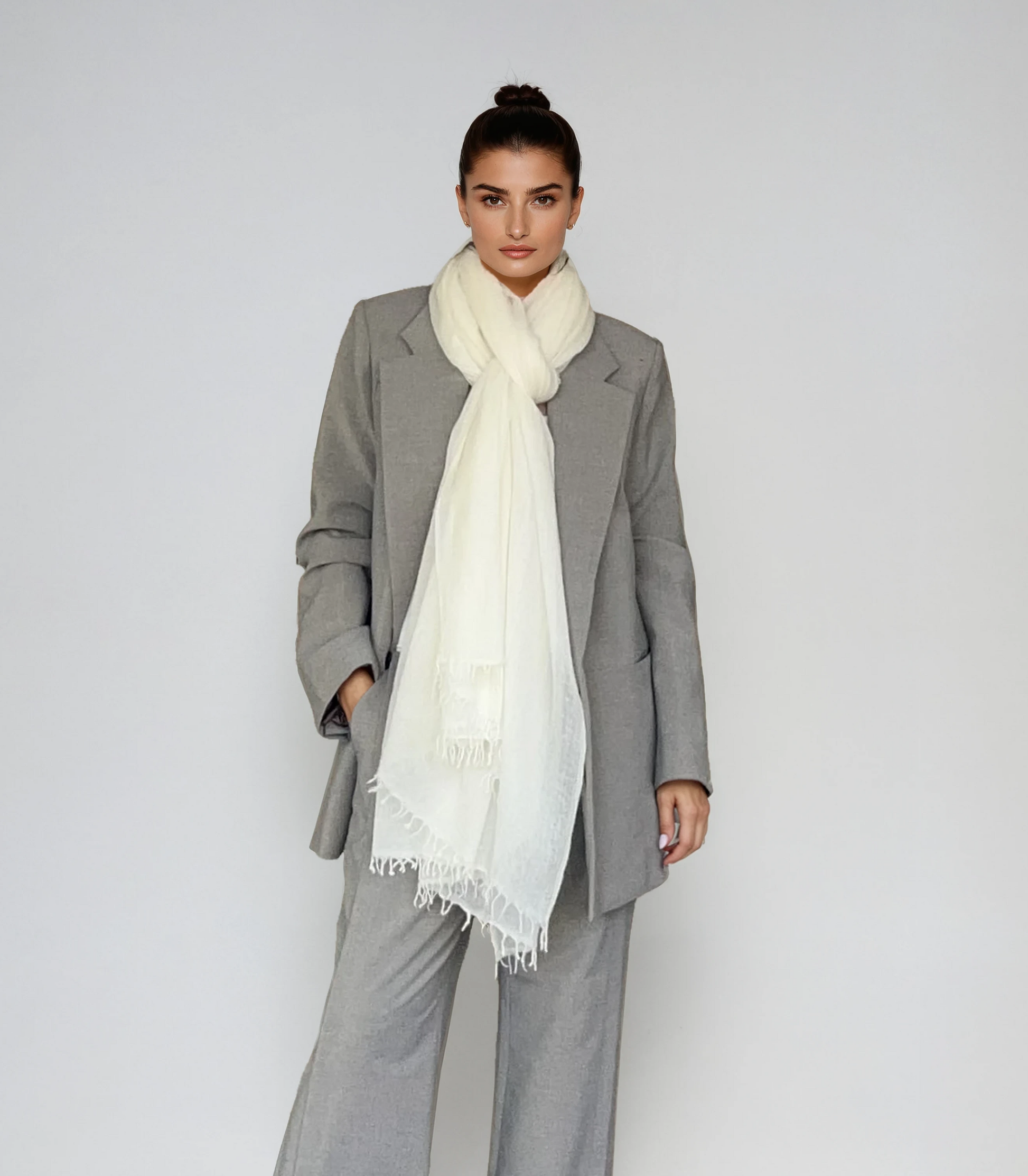 Woman wearing a gray suit with a white scarf on a plain background