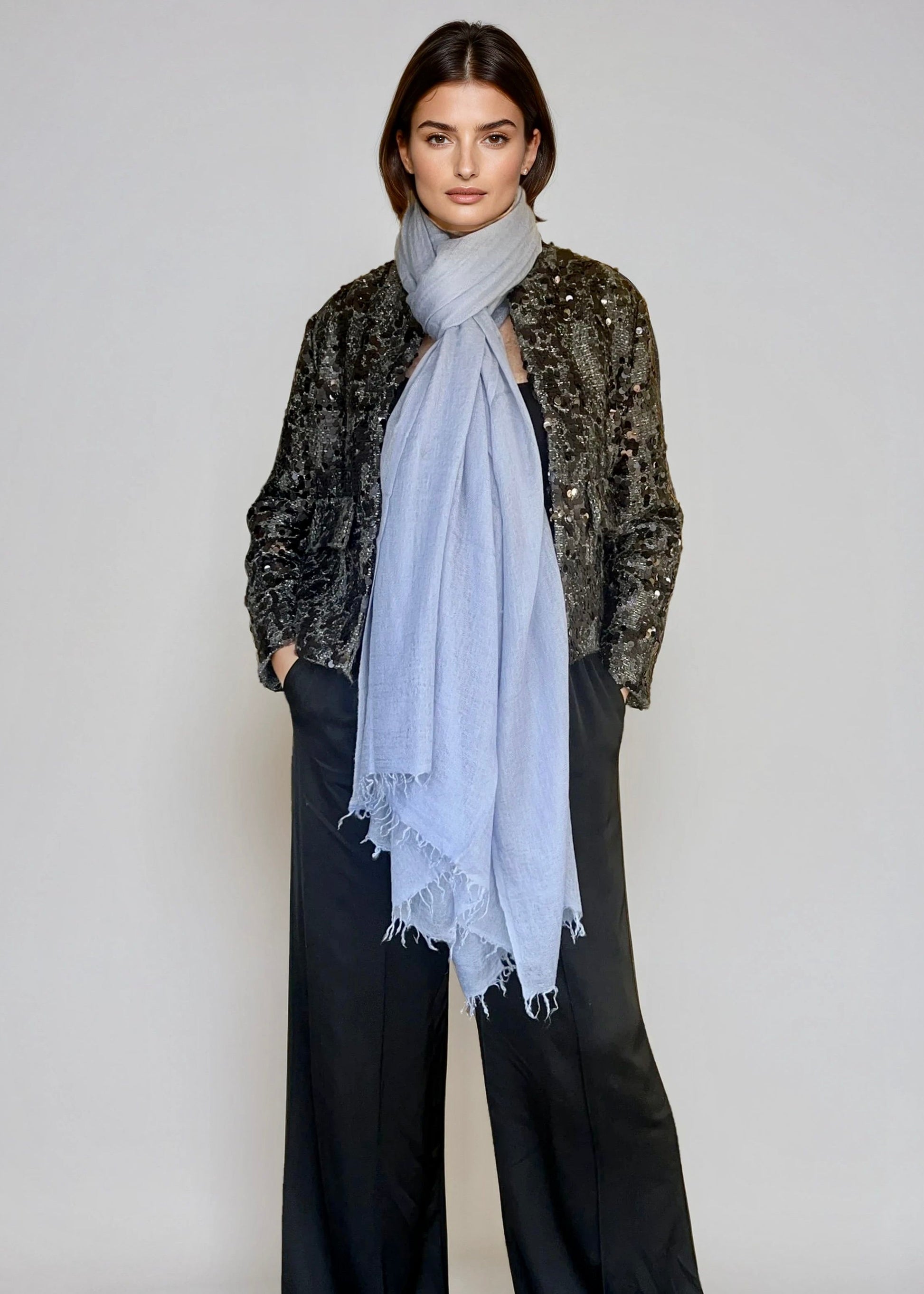 Woman wearing a light blue scarf and sequined jacket against a plain background