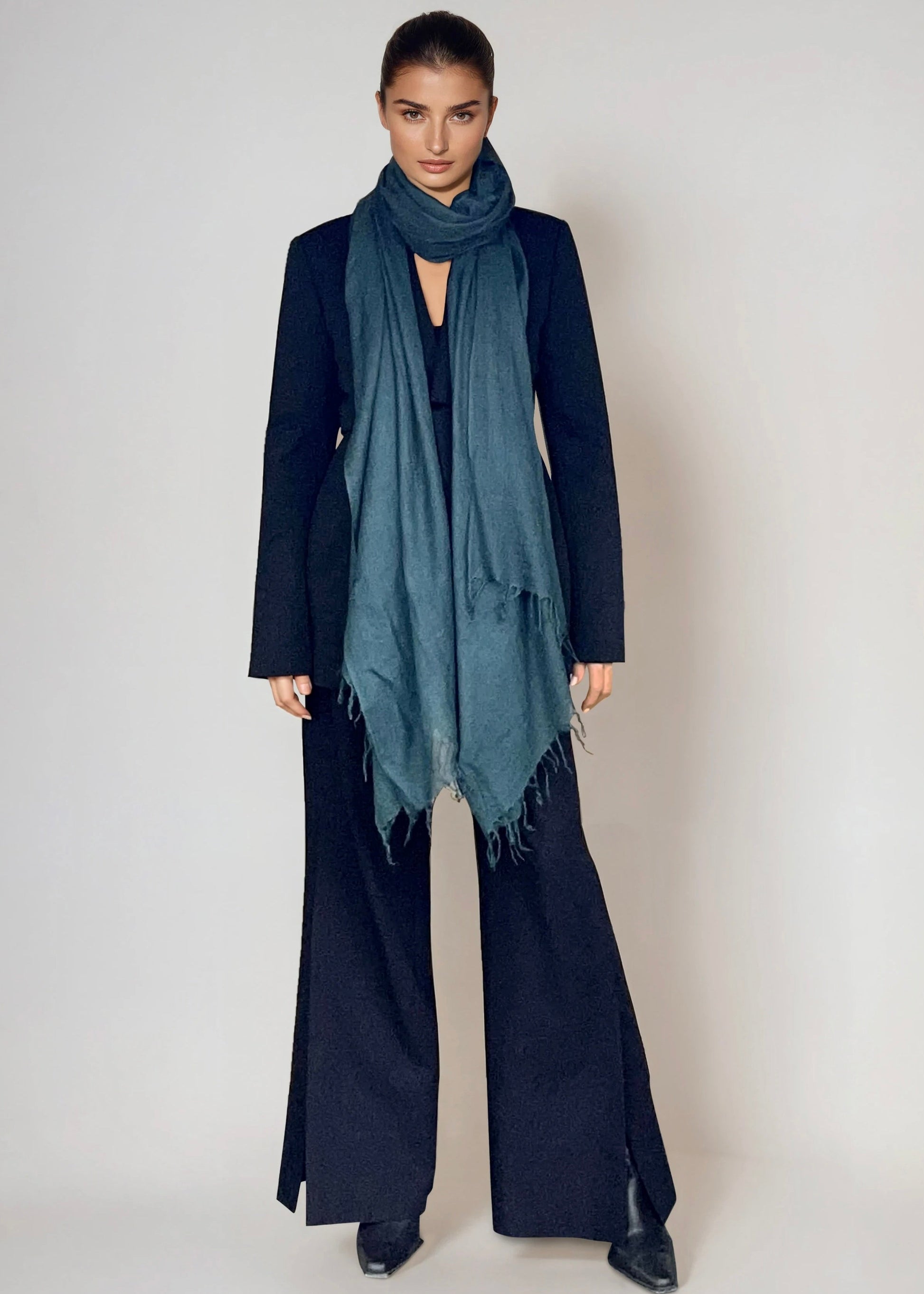 Woman wearing a dark coat, scarf, and pants on a plain background