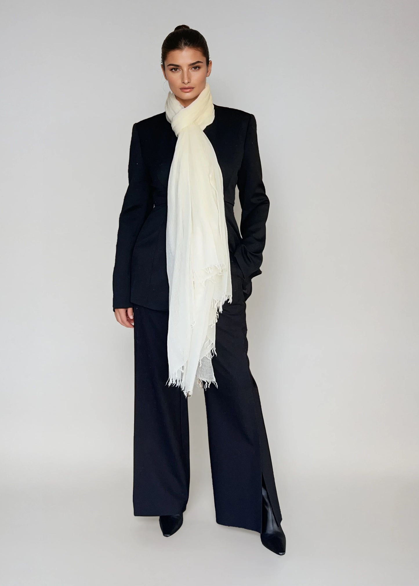 Person wearing a black suit with a white cashmere extra large scarf on a plain background