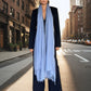 Woman wearing a long black coat and light blue scarf on a city street.