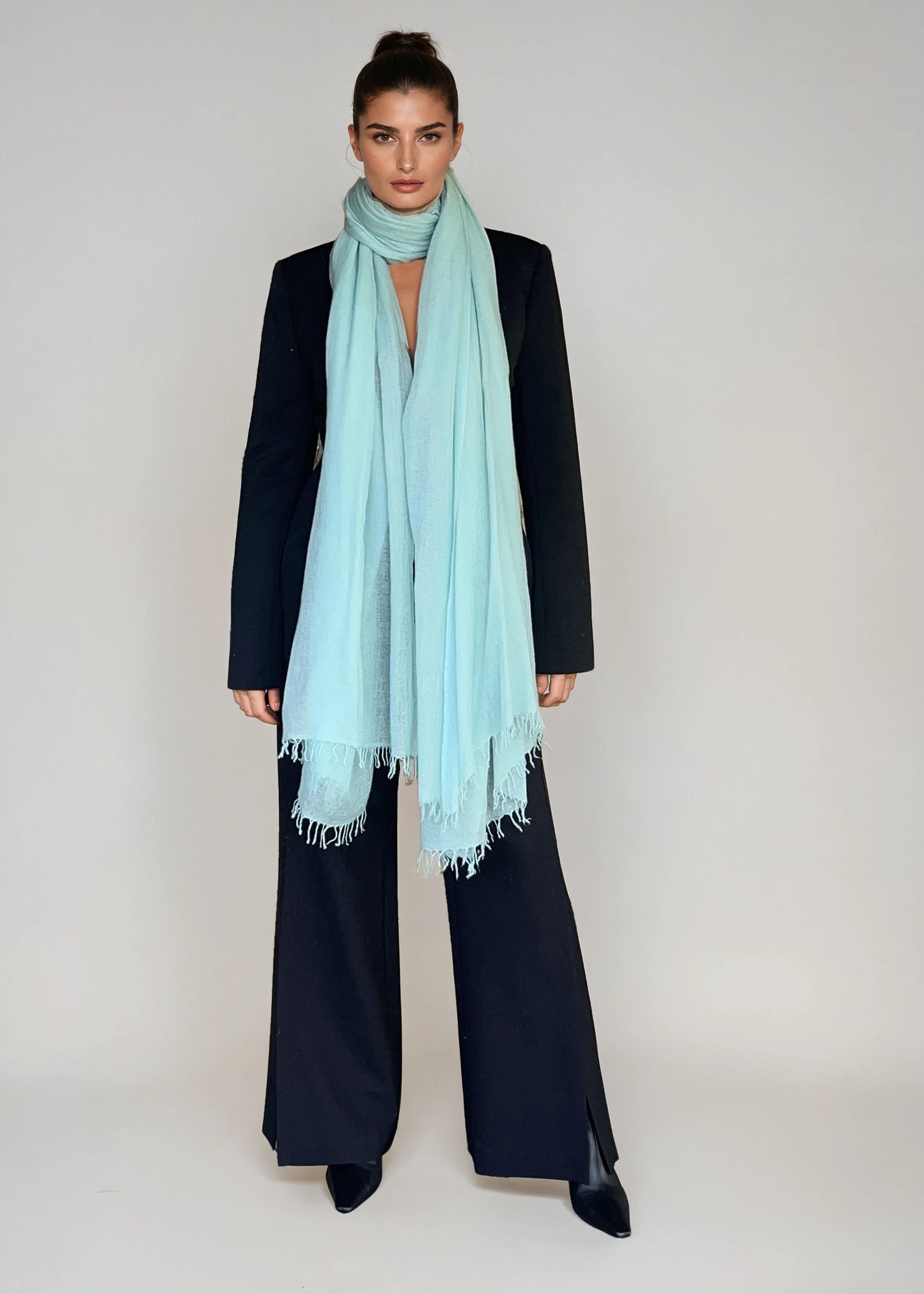Woman wearing a extra large, cashmere opal blue shawl on a plain background.