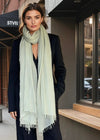 A woman wearing a celadon green oversized cashmere wrap and black suit.