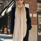 Woman wearing a beige extra large cashmere scarf and black suit on a city street.